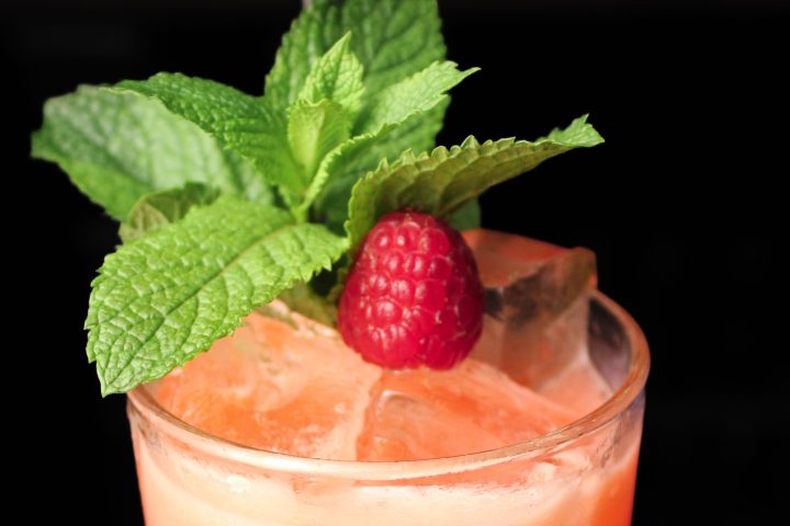Orange cocktail with raspberry, mint, and ice in a glass.