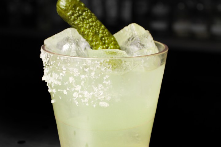 Cocktail with ice, pickle, and salted rim in a glass on a bar counter.